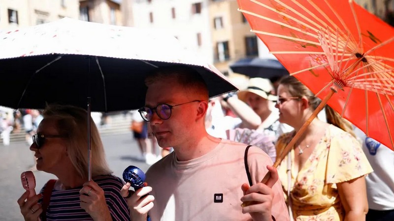 People use fans and umbrellas to protect themselves from heatwave